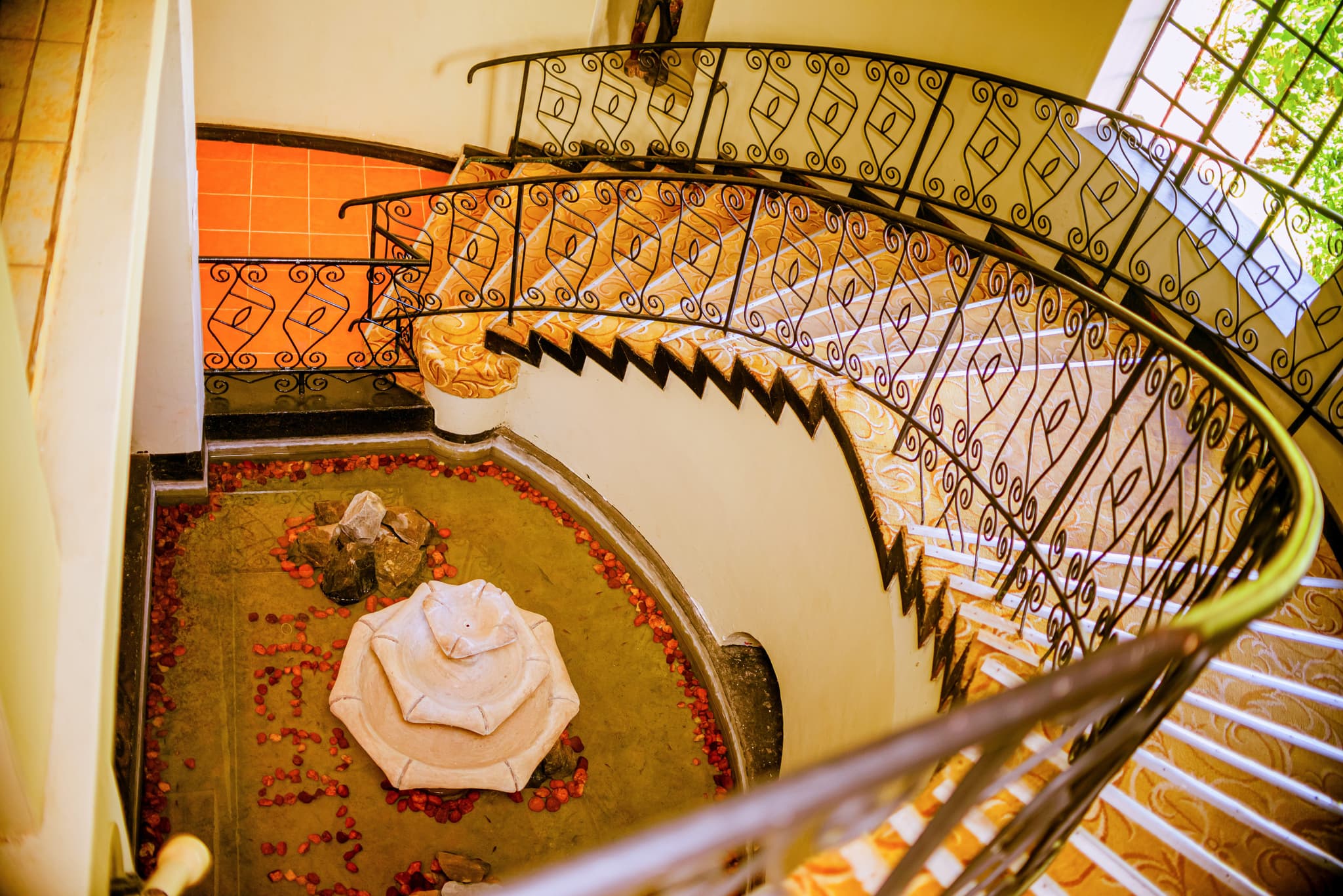 Elegant spiral staircase inside hotel with wrought-iron railing and decorative fountain.