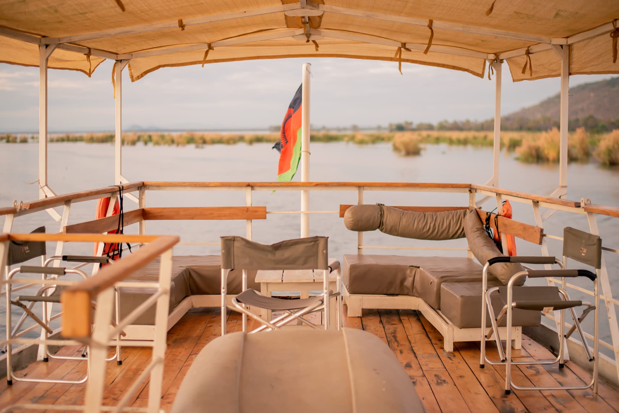 Open-air cruise deck with cushioned seating and panoramic views of calm waters and surrounding reeds.