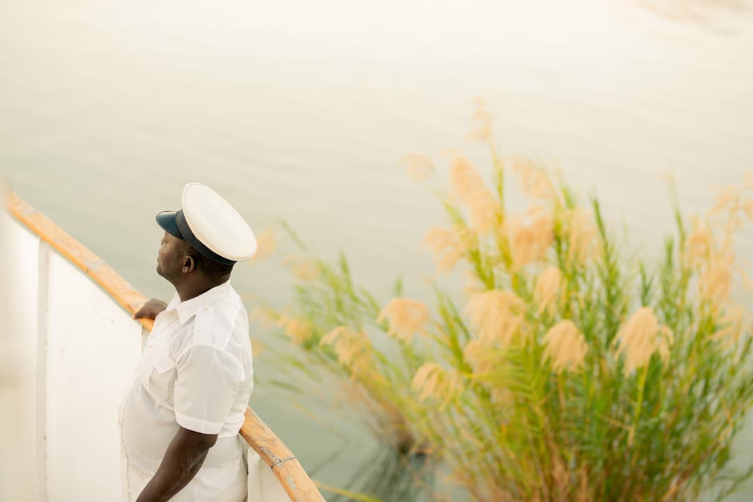 Boat captain in white uniform gazing over the calm waters of Lake Malawi on a serene afternoon cruise.