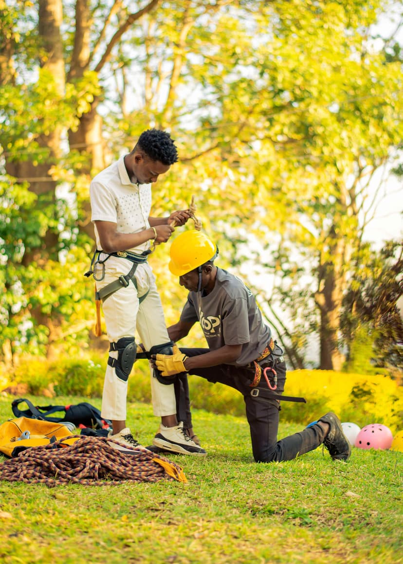 one person helping another adjust a zipline harness on a grassy field surrounded by trees.