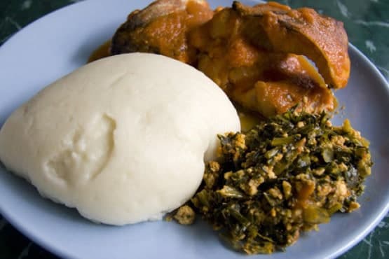 Traditional Malawian dish featuring nsima served with vegetables and stewed chicken on a plate. 